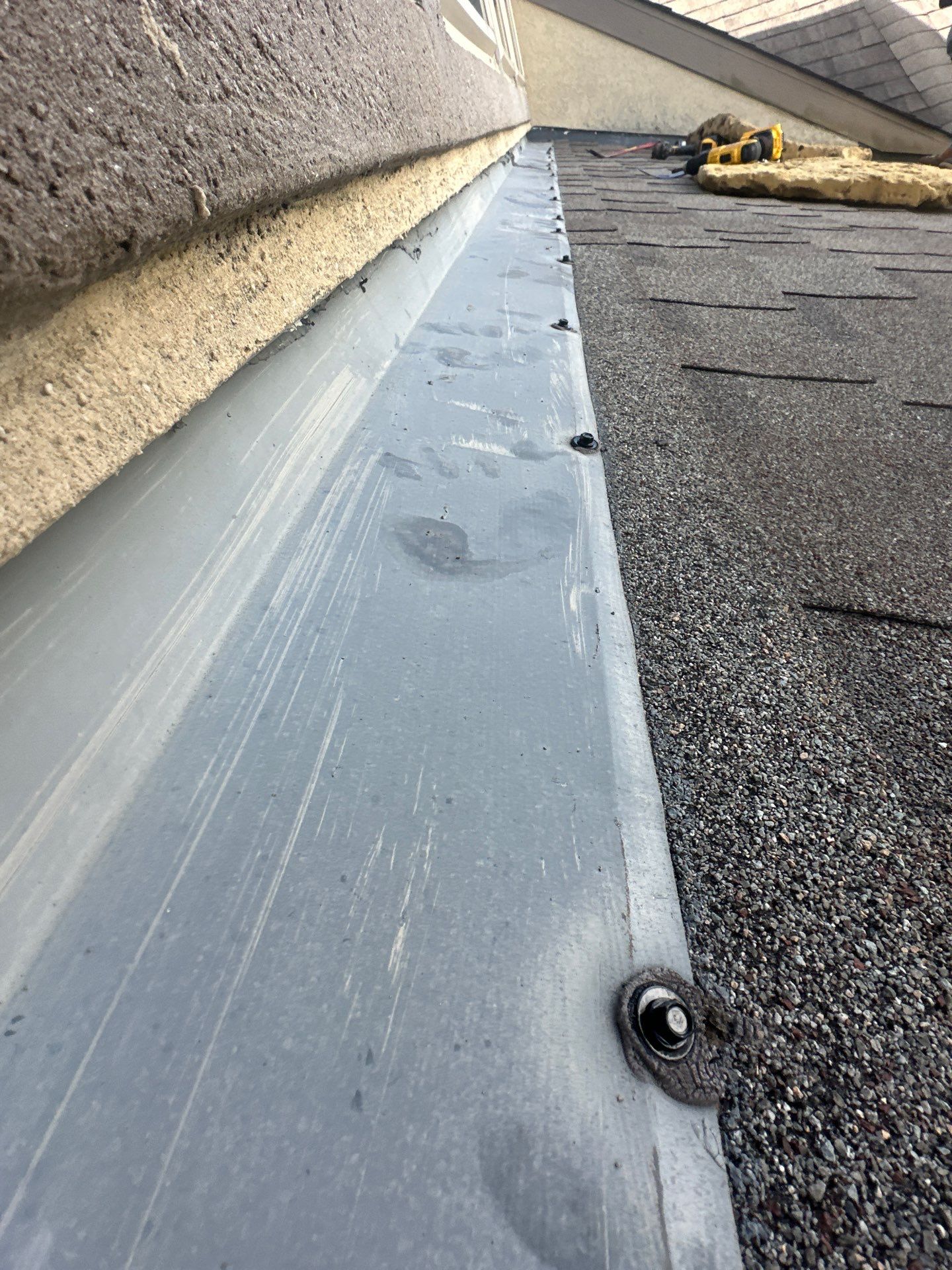 Close-up of a roof edge showing rubber-washered screws securing metal flashing, highlighting a permanent seal and proper roofing maintenance.